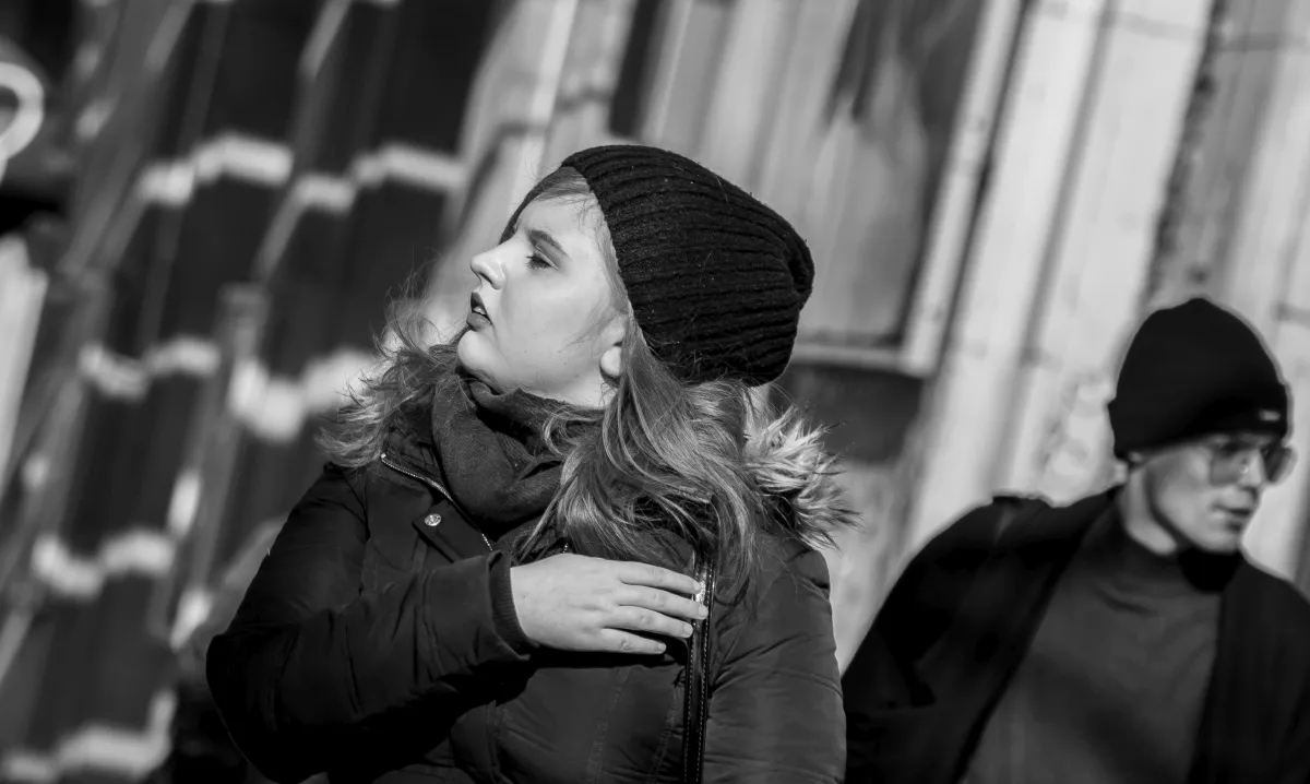 Young woman in a knit hat touching her shoulder while looking aside